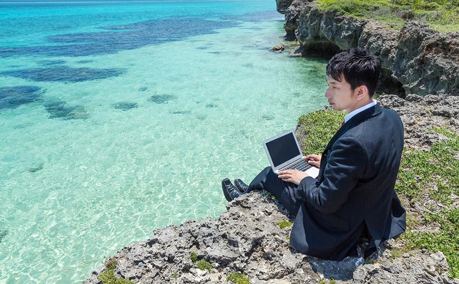 海でノートパソコンを使うスーツの男性