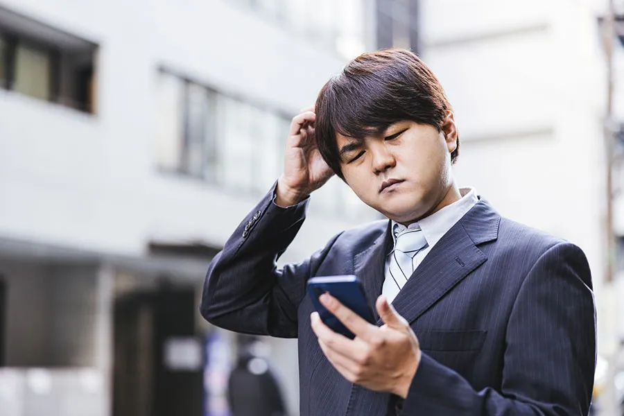 気まずい表情でスマートフォンを眺めるスーツの男性