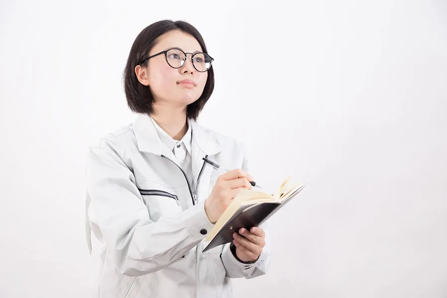 メモ帳にメモを取る作業着の女性