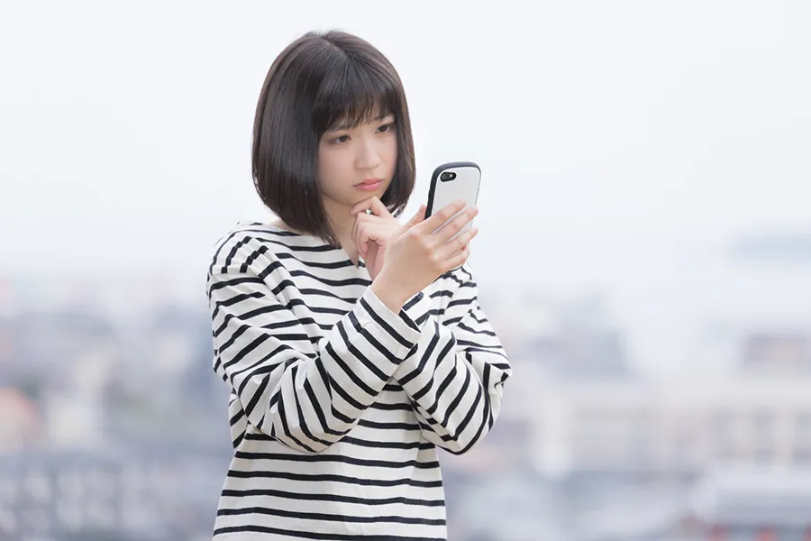スマートフォンを眺めて考え事をする女性